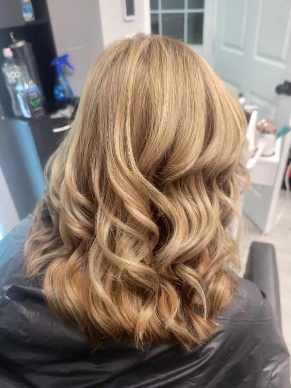 Back view of a person with long, wavy blonde hair with layers, sitting in a salon chair