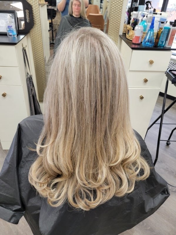 Back view of person with long blonde hair with voluminous waves in a salon setting