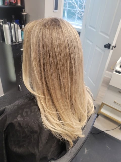 Rear view of a person with long, straight blonde hair in a salon setting with white doors and shelving in background